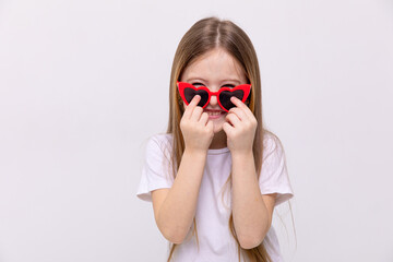 Wall Mural - Photo of pretty cute little girl dressed white casual t-shirt and red heart-shaped sunglasses, white color background. Summer concept. Copy space