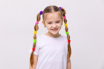 The little girl with braids of hair with multi-colored elastic bands, smiles broadly. Hairstyles for little girls. White isolated background.