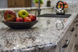 © StockUp - Close-up image featuring a bowl of fresh apples atop a granite countertop in a well-lit, stylish modern kitchen