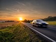 Motion blurred car driving on the asphalt road in rural landscape at sunset