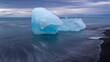 Ein kleiner hellblauer Eisberg spiegelt sich im Meerwasser, er liegt am schwarzen Sandstrand Diamond Beach bei Morgendämmerung