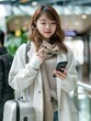 © romanets_v - Young Asian woman with suitcase using smartphone while waiting for her flight at airport terminal. Asian businesswoman on business travel. Lifestyle and technology. Travel and vacation concept