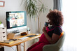 © Jimena Roquero/Stocksy - Pregnant woman in video call in home office drinking tea
