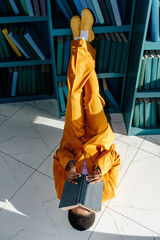Anonymous woman lying on floor and covering face with book in library