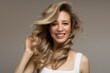 young blonde woman with curly beautiful hair smiles on a gray background