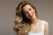 young blonde woman with curly beautiful hair smiles on a gray background