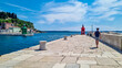 Tourist man walking along picturesque harbor of coastal town Piran. Walking next to the lighthouses overlooking the Adriatic Mediterranean Sea. Summer scene in small port.