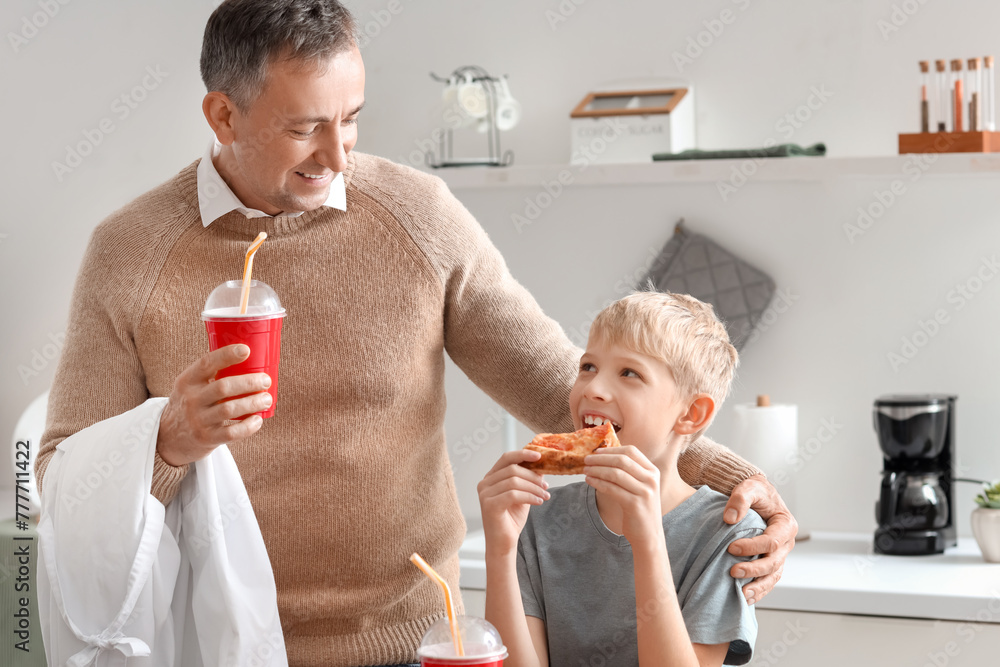 Mature doctor with his little son eating pizza in kitchen