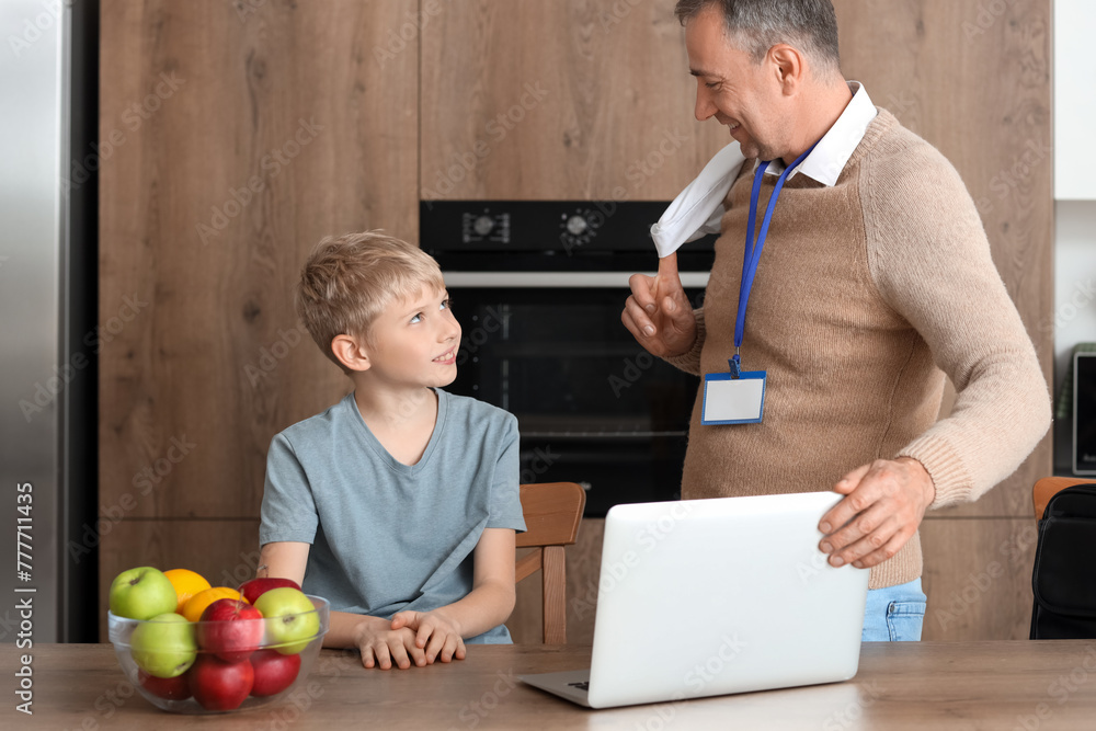 Mature doctor with laptop and his little son in kitchen