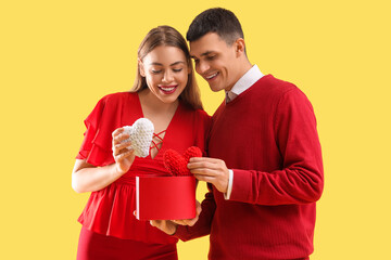 Poster - Young couple in love with hearts and gift box on yellow background. Valentine's Day celebration