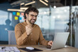 © Liubomir - Cheerful businessman with glasses celebrating a success while working on his laptop in a modern office environment.