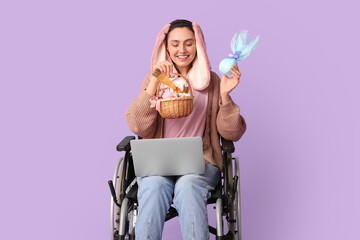 Wall Mural - Happy female freelancer in wheelchair with Easter basket, chocolate egg and laptop on purple background