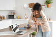 Hurrying African-American businesswoman with notebooks and wristwatch curling hair in kitchen