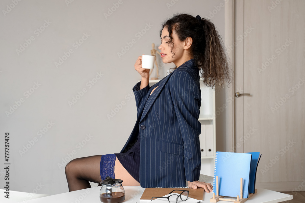 Sexy African-American secretary drinking coffee on table in office