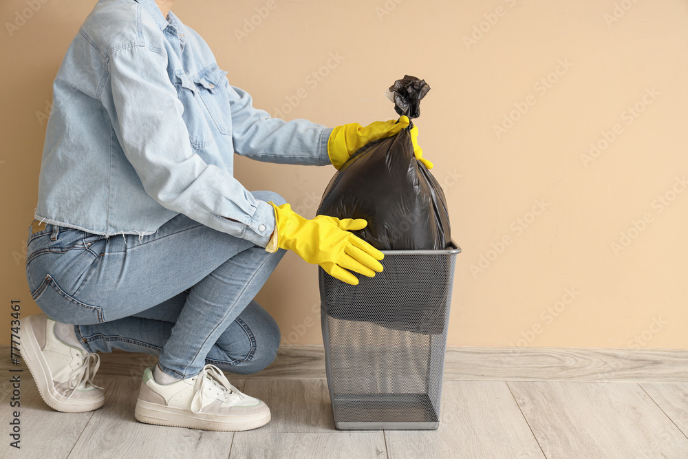 Woman taking garbage bag from trash bin near beige wall