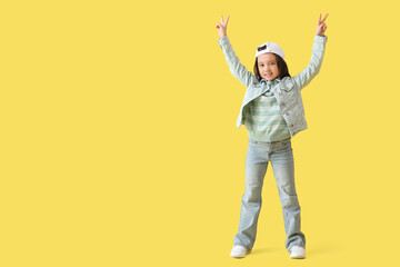 Wall Mural - Portrait of fashionable little girl showing victory gestures on yellow background