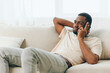 © SHOTPRIME STUDIO - Happy African American man sitting on a black sofa, using his mobile phone for a video call The modern apartment creates a comfortable backdrop as he confidently chats and relaxes With a smile on his