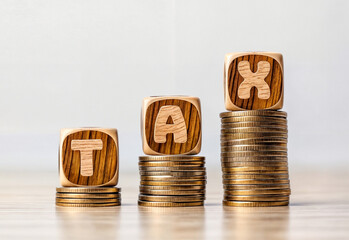 Stacks of coins with wooden blocks spelling out text word TAX on top of each stack