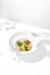 Wall Mural - Seafood risotto with scallops and cauliflowers on white plate. Creamy risotto with sea scallops and cauliflowers. Italian risotto with sea scallops on light background with shadows of leaves