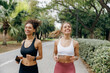 Two smiling women in sportswear are running on natural parkland background. Active lifestyle concept
