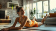 Relaxed woman in an orange sports top stretching on a yoga mat at home.