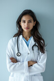 Fototapeta  - An Indian young female doctor in a white lab coat with a stethoscope exudes confidence and professionalism against a soft blue background