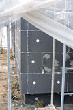 Fototapeta Zwierzęta - A wall of a house covered with EPS graphite polystyrene boards for thermal insulation, a scaffolding and building safety scaffolding net, anchors, an exterior wall mounted water faucet