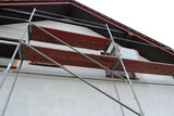 Fototapeta Zwierzęta - A scaffolding near a wall which is covered with prime before rendering exterior walls, windows and windowsills covered with a protective film, bottom view