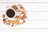 Fototapeta Mapy - Topview of coffee in a white cup surrounded by chestnuts, hazelnuts, star anise and cinnamon on a grey planked wooden background. Autumn still life with a hot drink