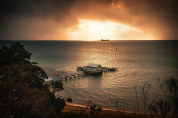 Wall Mural - The sunrise view of a pier in Millionaire's Walk in Mornington Peninsula with a ship sailing in the sunlight in the distance