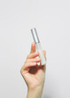 hand holding transparent bottle with a brush for eyelash and eyebrow care serum