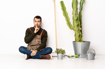 Poster - Gardener man sitting on the floor at indoors showing a sign of silence gesture putting finger in mouth