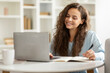 © Home-stock - Positive cheerful young woman student using laptop and taking notes, attending webinar, have online training at home interior