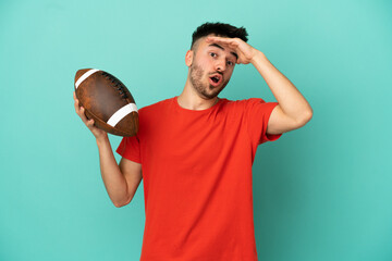 Wall Mural - Young Caucasian man playing rugby isolated on blue background doing surprise gesture while looking to the side