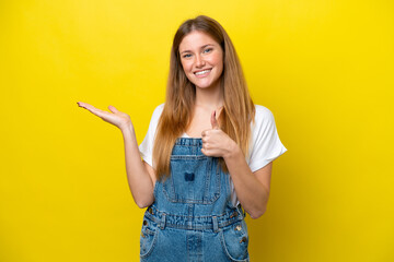 Canvas Print - Young caucasian woman isolated on yellow background holding copyspace imaginary on the palm to insert an ad and with thumbs up