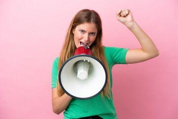Wall Mural - Young blonde woman isolated on pink background shouting through a megaphone to announce something