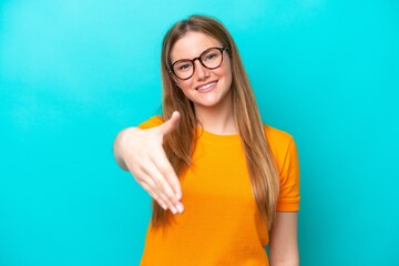 Wall Mural - Young caucasian woman isolated on blue background shaking hands for closing a good deal