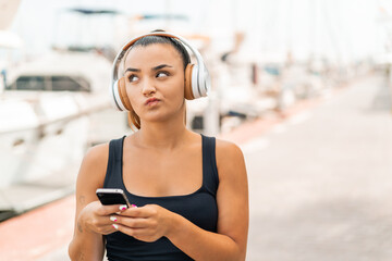 Poster - Young pretty woman at outdoors listening music with a mobile and thinking