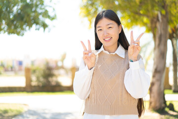 Wall Mural - Pretty Chinese woman at outdoors showing victory sign with both hands