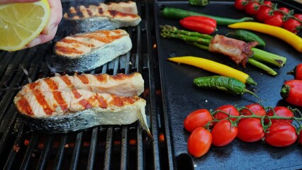 Wall Mural - Salmon fish steak on grill with vegetables. Chef hand squeezes lemon on fish steak grilled. Slow motion. Close up