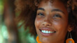 Photo of cheerful beautiful black woman with brown curly hair and beautiful smile with white teeth on nature background. Natural woman beauty concept. Selective focus 