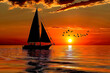 Monochrome orange black sailboat silhouette on the ocean birds flocked overhead with sunset on the horizon