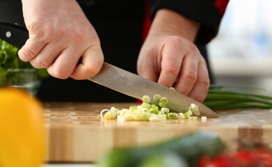 Wall Mural - Cook holds knife in hand and cuts on cutting board green onions for salad or fresh vegetable soup with vitamins. Raw food and vegetarian recipe book in modern society popular concept.