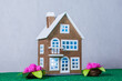 There are flowers near a brown toy house with blue light in the windows