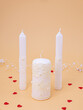Still life: three white wedding candles on a soft orange background with red hearts