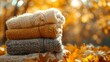 Pile of warm handmade jumpers under golden foliage, soft focus