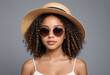 portrait of black American biracial girl with curly hair wearing a summer sun hat wearing stylish sun glasses posing on a perspective angle on a grey background