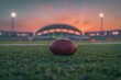 Football resting on field, stadium arcs in background, twilight, symbolizing anticipation and competition
