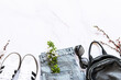 Fashion spring and summer composition with trendy sneakers, leather backpack, blue jeans and sunglasses on white marble background decorated with blooming apricot twigs top view with copy space.