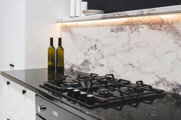 Poster - A black stove top with four burners and a marble counter top. A bottle of wine is on the counter next to the stove, Kitchen interior
